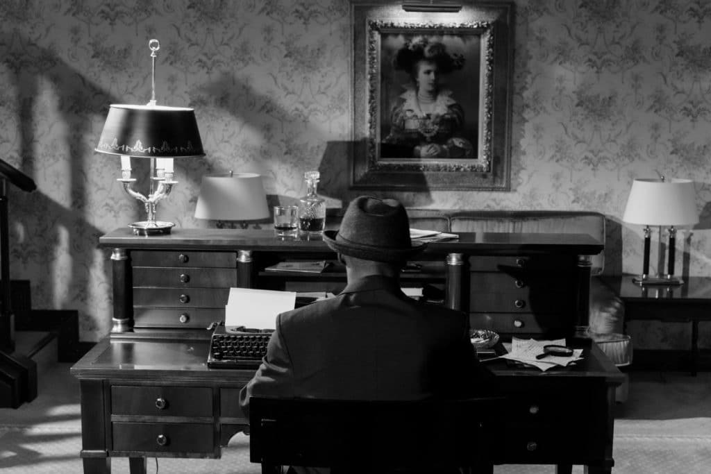 The back of a man sitting at a desk in a black and white picture.
