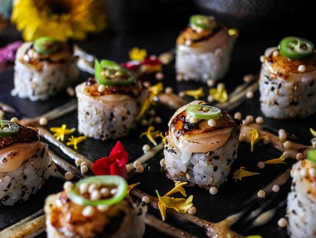A close up of sushi presented with yellow flowers and other decorative details.
