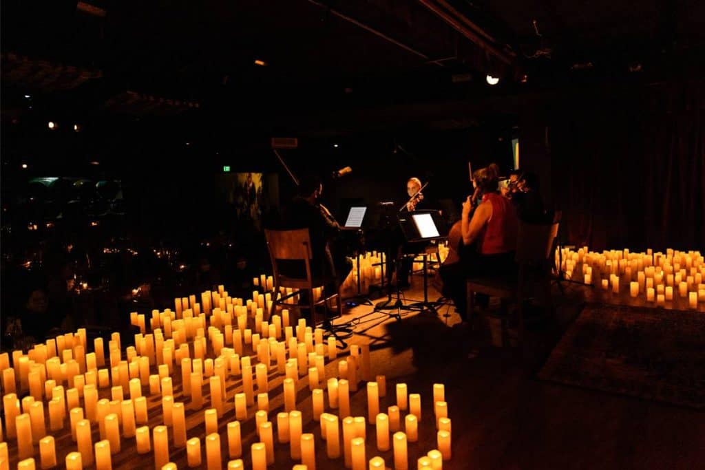 A string quartet performing on a stage with hundreds of candles around them at a Coldplay Candlelight concert in Atlanta.