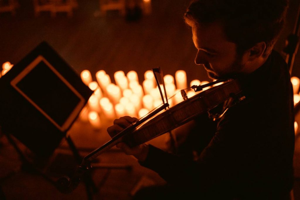 A man playing the violin with candles in the background.