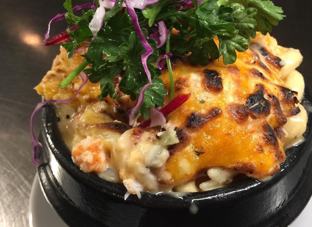 A close up of a pot of mac and cheese topped with some salad leaves. 
