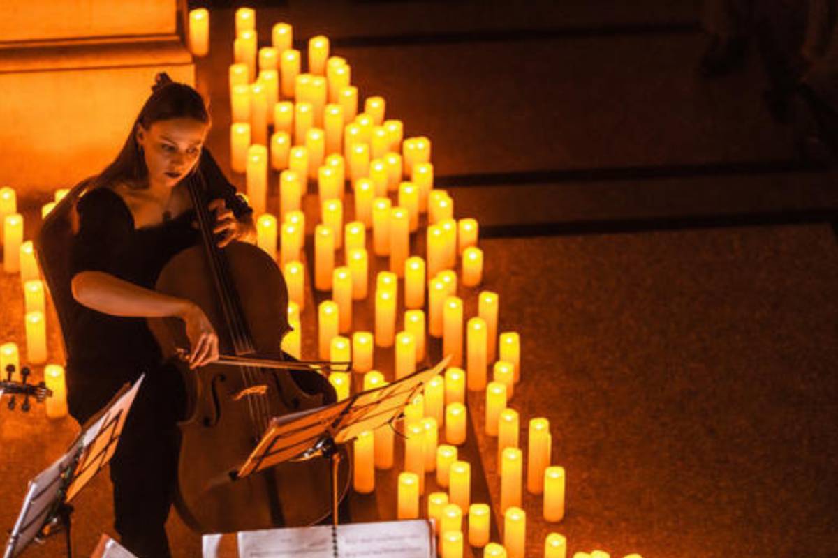 A woman playing the cello with a river of candles glowing alongside her.