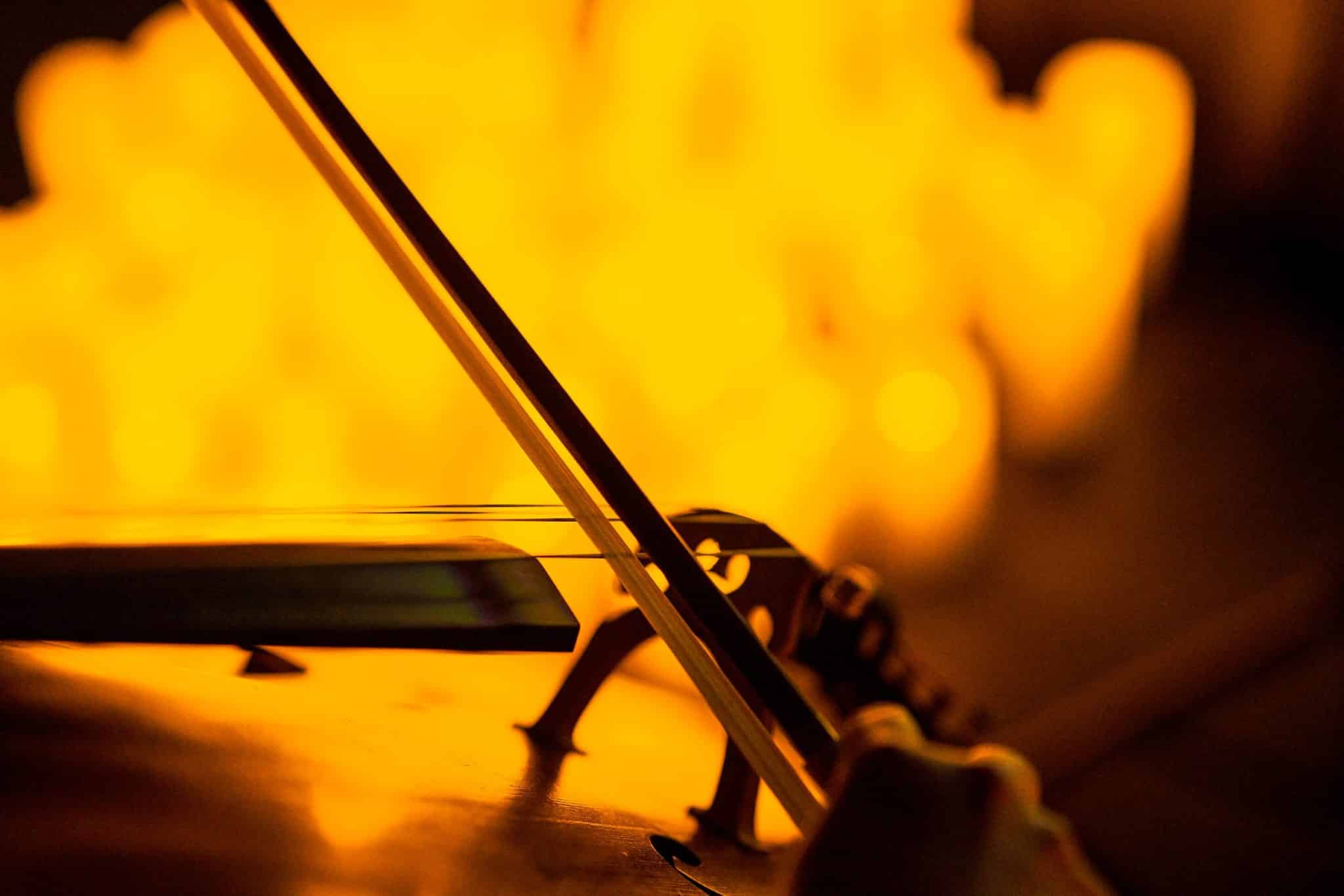 A close-up of a bow being used to play a string instrument with the blurry glow of candlelight in the background.