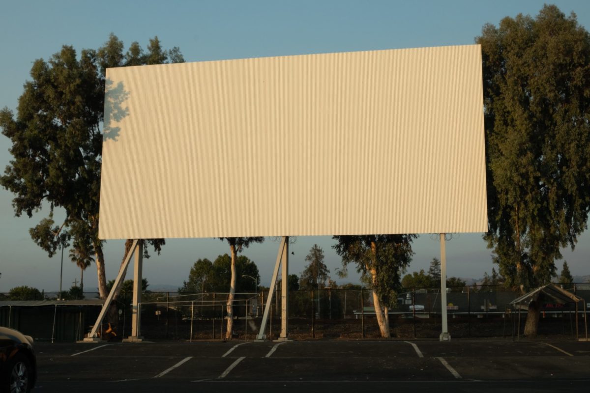 A large screen set up for a drive-in theater with the sun shining on it and trees visible in the background.