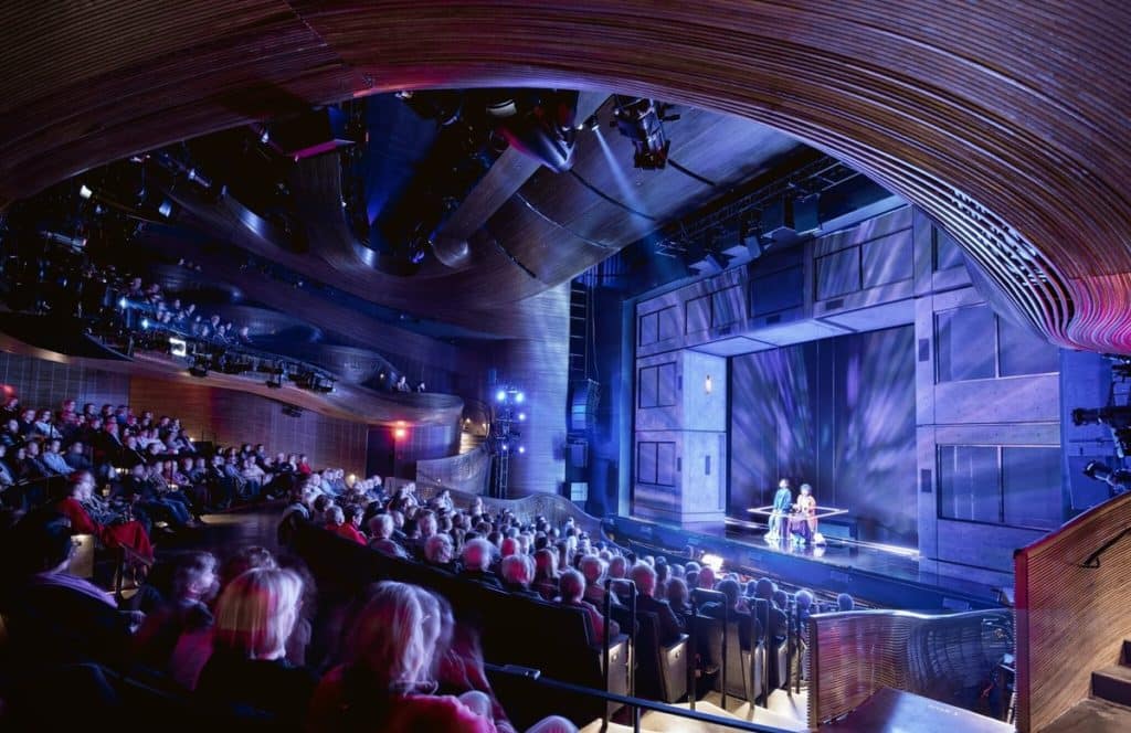 Inside the Alliance Theatre in Atlanta where a performance is taking place and the lighting is purple and blue and the image shows the stage from the audience.