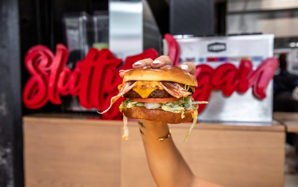 Hamburger being held in front of Slutty Vegan sign