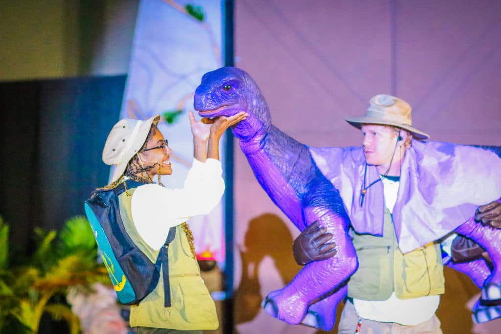 A woman pets a dinosaur puppet that a man is holding
