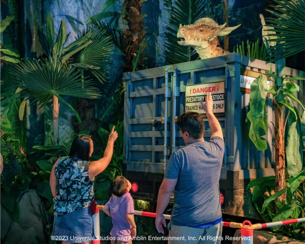 A family pointing at a dinosaur inside of a huge shipping container at Jurassic World: The Exhibition