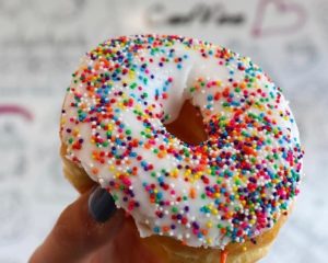 An iced ring donut covered in sprinkles.