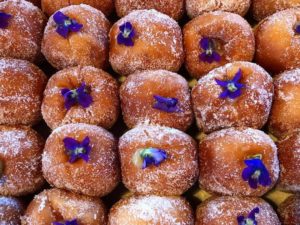 A tray of filled donuts topped with purple flowers.