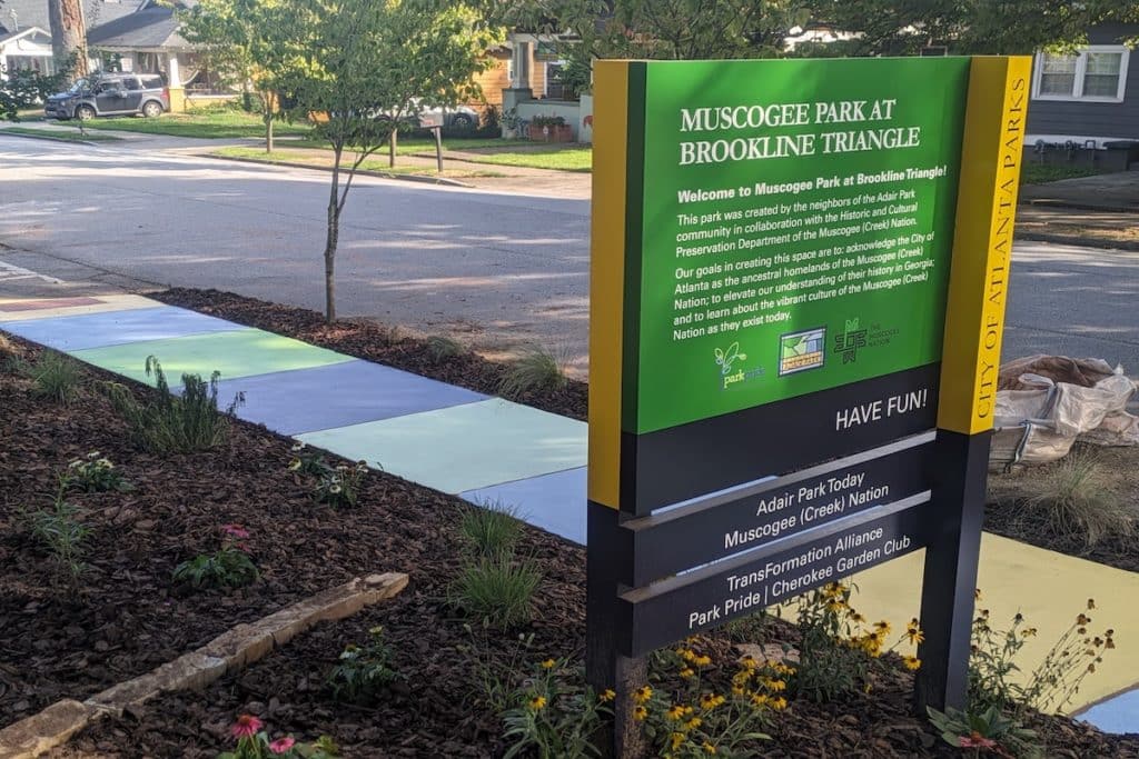 Photo of a green and yellow informational sign. A colorful sidewalk is in the background.