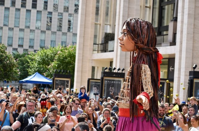 Giant puppet of a Syrian refugee girl, Little Amal, walks through a crowd of people